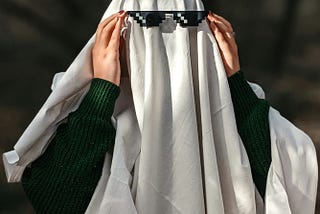 Image of a person covered in a white sheet as a simple ghost costume with black sunglasses on.