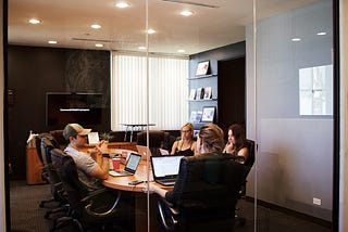 Four people around a table in a conference room with glass walls.