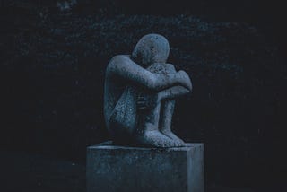 A statue of a person crouched in a fetal position with their head buried in their knees