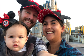 Two adults and a child pose in front of Cinderella’s castle in Disney World