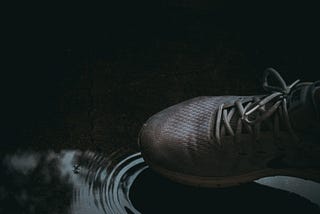 Sepatu putih lusuh sedang menjajakkan kaki ke kubangan air hujan