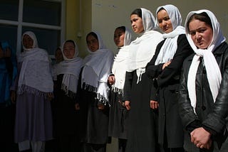Afghan schoolgirls wearing black dresses and white head scarves. Lined-up to get into class.