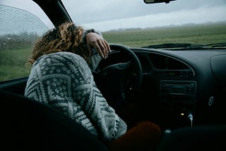 Woman has her head on the steering wheel of an unknown car, as if she’s crying.