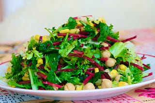 A plate of green salad leaves with grated beetroot and chickpeas.
