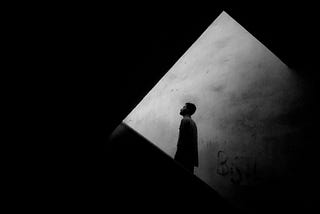 black-and-white image of the silhouette of a man against a square lit wall