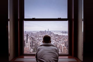 A young man looking out of an apartment window.