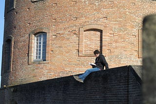 A reader sitting on the eadge of a wall to reading to transform his perspective