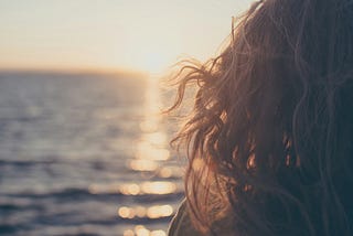 Woman on right side of frame with curly long hair watching sunset