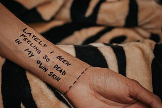 A hand with text written as: LATELY I BEEN FEELING SO DEAD IN MY OWN SKIN