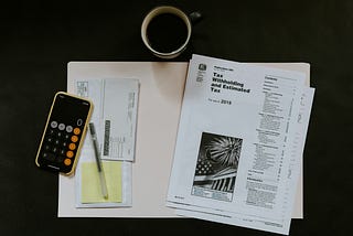 Tax documents, phone with calculator and cup of coffee viewed from above against a black background
