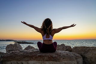 Woman at the beach with a yoga pose to make her day feel better