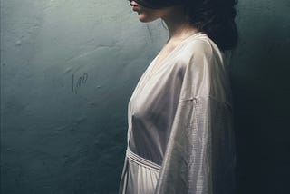 Beautiful brunette-haired woman in profile view wearing a white robe in front of a cobalt blue wall.