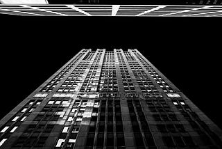 Black and white picture of a skyscraper, photographed from the bottom looking up at the building reaching to the sky.