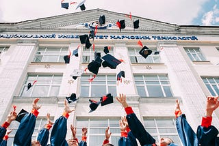 students throwing graduation caps into the air in front of a college building