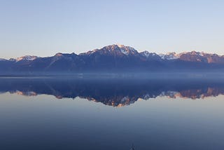 A mountain range with a clear blue sky background and clear water showing a pristine reflection of the mountain.