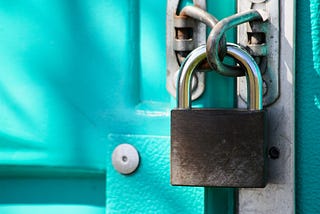 A rusted silver padlock holds together two bright teal doors.