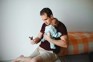 Image of man holding newborn and his phone.