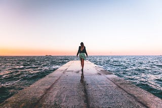 The picture shows a woman walking along a pier at the beach depicting a financially free life.