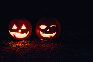 Two smiling pumpkins sitting together, glowing in the dark.