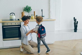 A mother standing in the kitchen with her son, wishing him luck for his first day of school.