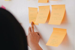 A person is pointing to a sticky note in a board full of sticky notes