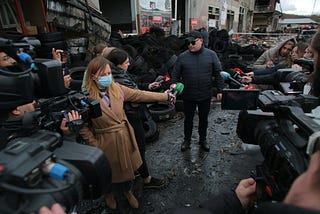 Video journalists and reporters around a man with car tires in the background