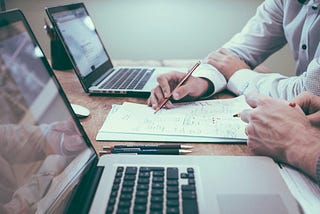 simple image of a desk with laptops and people working on the laptops