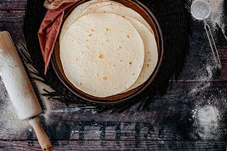 a bowl of fresh flour tortillas, with a rolling pin at the left.