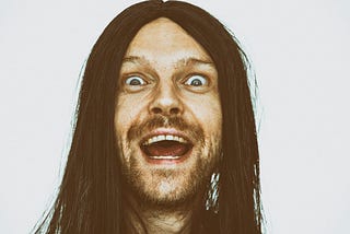 Photo of a crazy-eyed man with long, greasy hair, his expression manic.