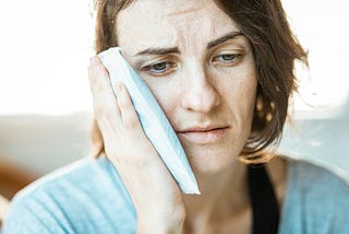 A woman who looks like she’s in pain holds an ice pack to her cheek.
