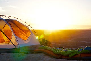 A tent in the outdoors facing a fresh sunrise