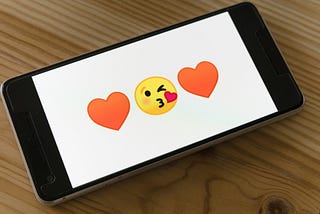 A mobile phone showing two hearts and a kiss emoji