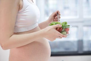 A pregnant woman holding a bowl of salads.