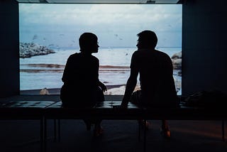 The sillouette of two people sitting in front of a large window