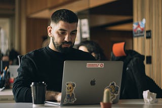 Bearded man wearing a black sweater typing on a portable computer in an office