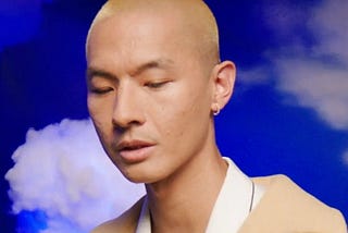 A headshot of KevJumba looking downwards in front of a cloud-printed background