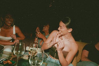 A group of women laughing and talking together at a dimly lit dinner party