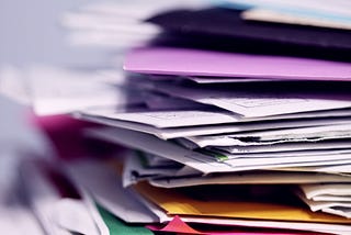 stacked papers and file folders in different colours. All askew. zoomed in view. Some background blur.
