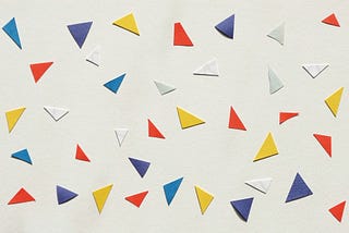 Many red, blue, yellow and white paper triangles scattered on a larger sheet of paper.