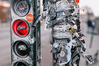 Bicycle traffic lights, red light is on for turning left. Light pole and light is covered with ramones stickers, signs and grafitti.