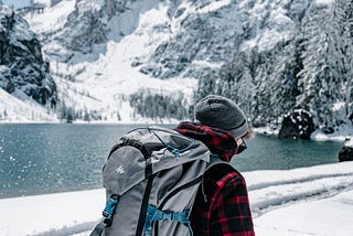 A backpacker hiking in winter next to a lake.