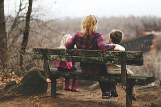 A woman sits with two kids on a bench.