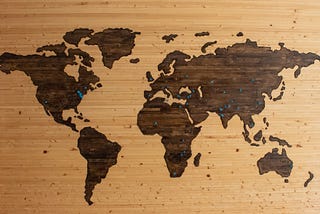 An image of a wooden world map with pins on it.