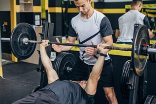 A spotter assisting someone with his lift on the bench press.