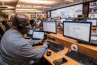 A responder wearing a headset, sitting in front of multiple computer screens