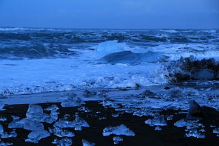 a lovely night landscape of blue ocean and sky with ice strewn on the ground