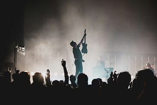 In a picture at a rock concert, a band member is holding up his guitar to the crowd