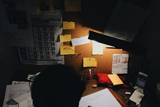 Working at a dark, untidy desk, late at night.