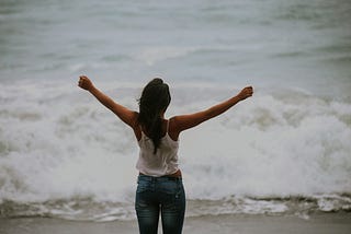 A woman facing a wave with her arms outstretched