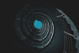 Photo of a repeating spiral staircase, viewed from below (I think), looking up to a blue sky